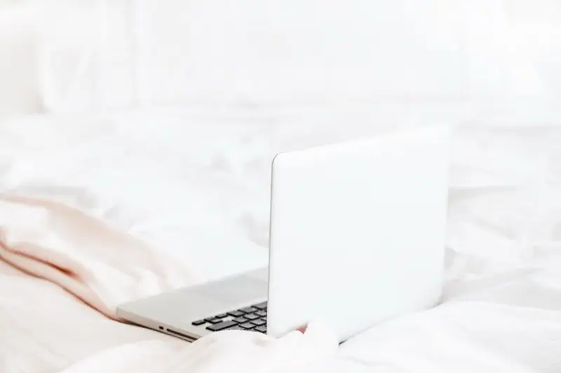 Woman using a laptop while sitting on white bedding