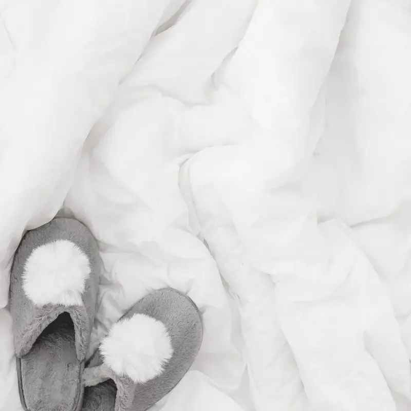 Gray slippers with white pom-poms on rumpled white bedding