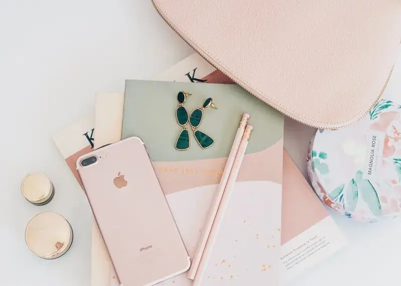 Pink phone, cosmetics, and accessories arranged on a desk