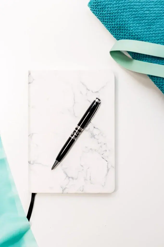 Marble notebook and pen beside a turquoise towel