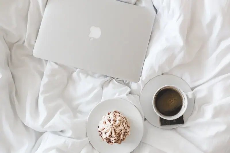 Laptop, coffee, and dessert on white bedding