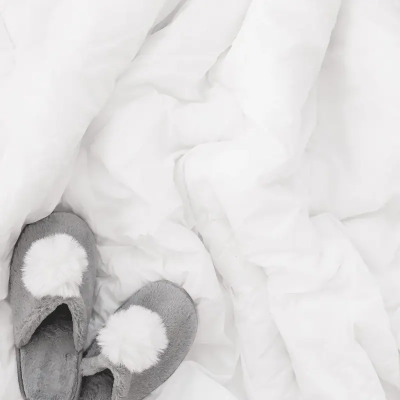 Gray slippers with white pom-poms on rumpled white bedding