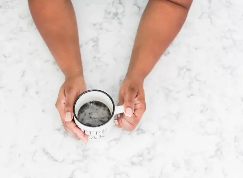 Hands holding a coffee mug over a white marble surface