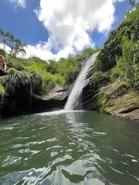 A waterfall pouring into a green river pool under blue sky