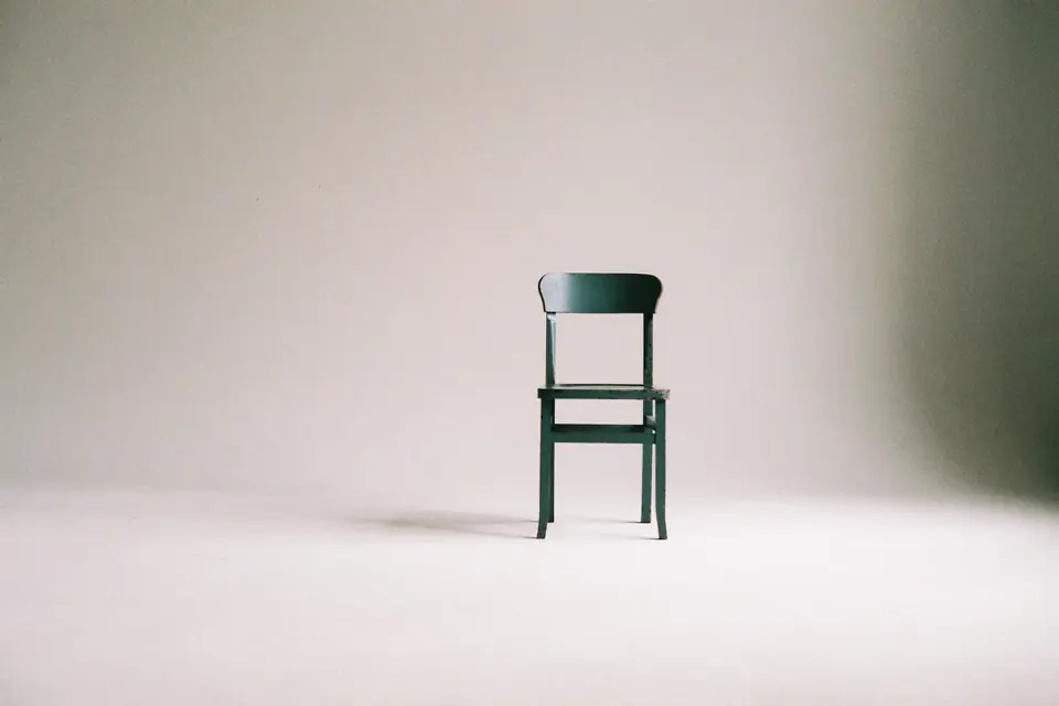 A single green wooden chair against a soft pale wall