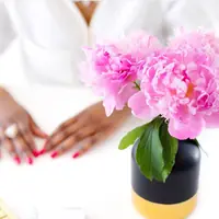Hands with pink nails beside a vase of bright pink peonies