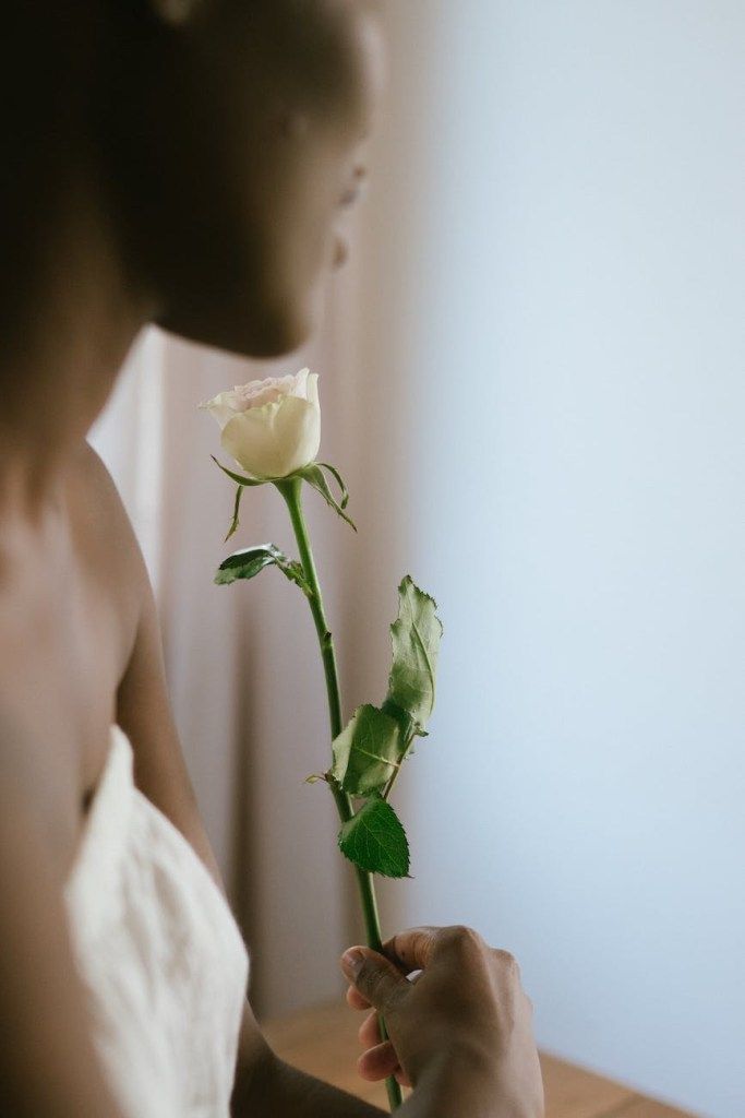 Woman holding a white rose by a window