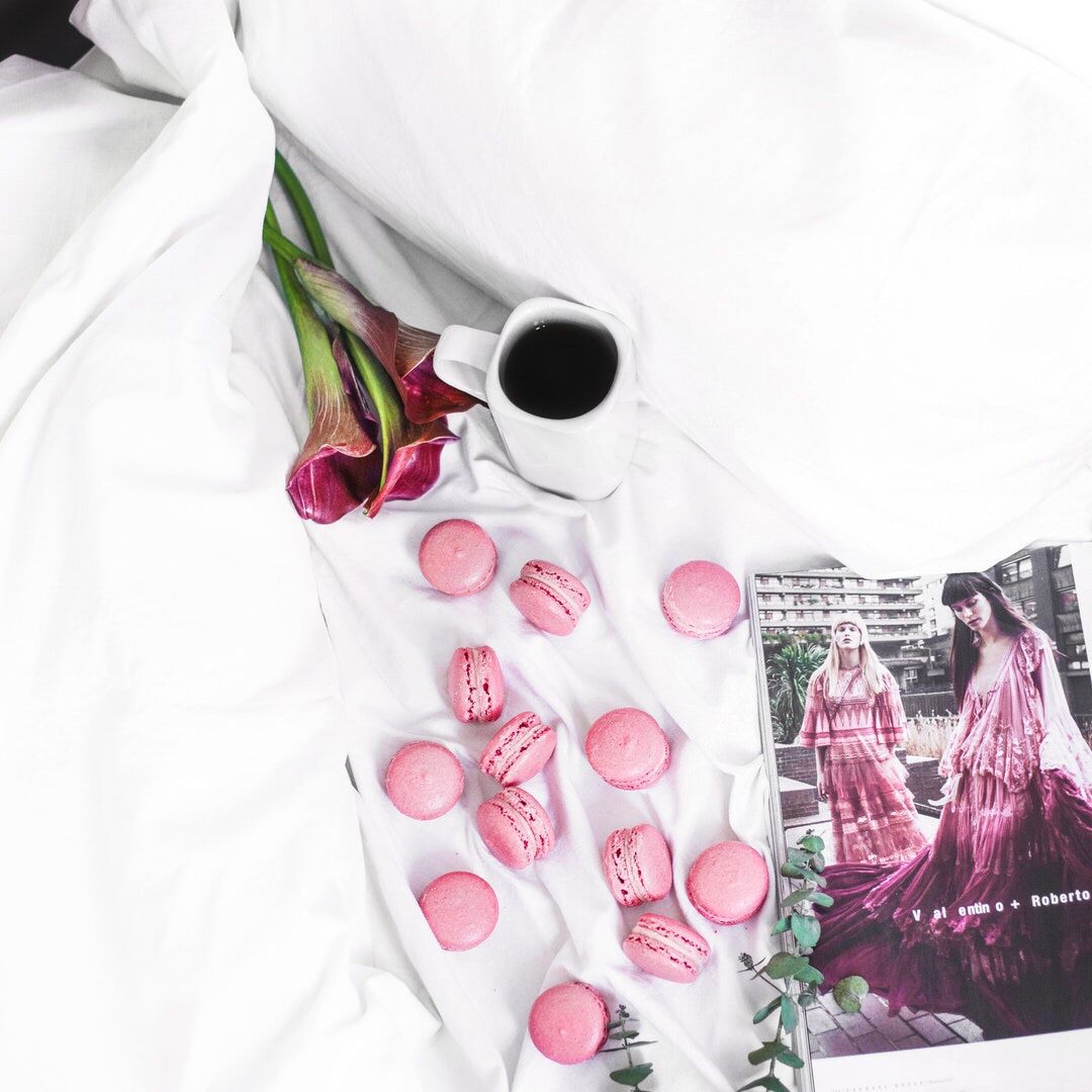 Fashion magazine, coffee, roses, and pink macarons on white bedding