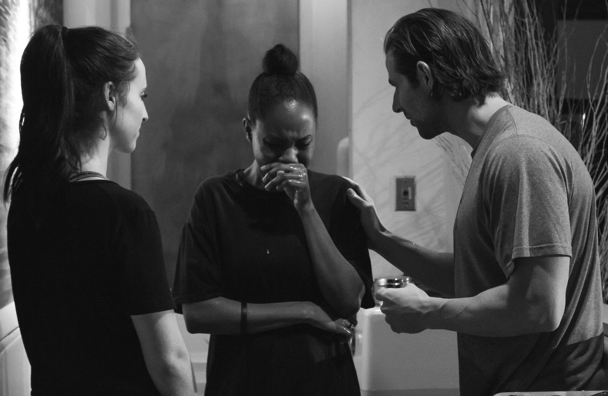 A woman with wet hair covering her face in tears while two people stand close, one resting a hand on her shoulder