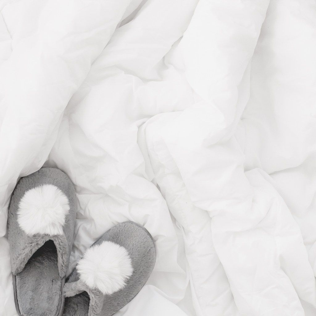 Gray slippers with white pom-poms on rumpled white bedding
