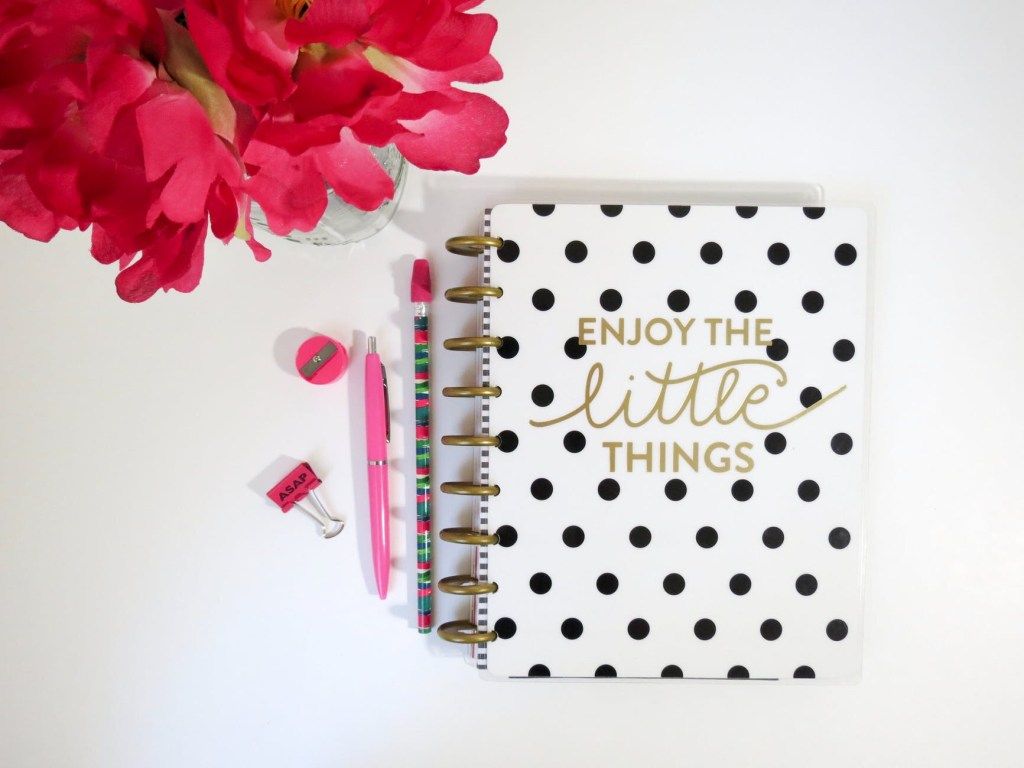 Notebook reading “Enjoy the little things” beside pink flowers