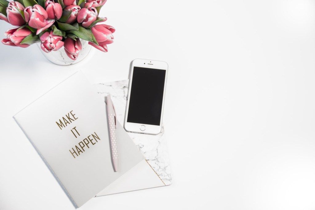 Phone and notebook reading “Make things happen” beside pink flowers