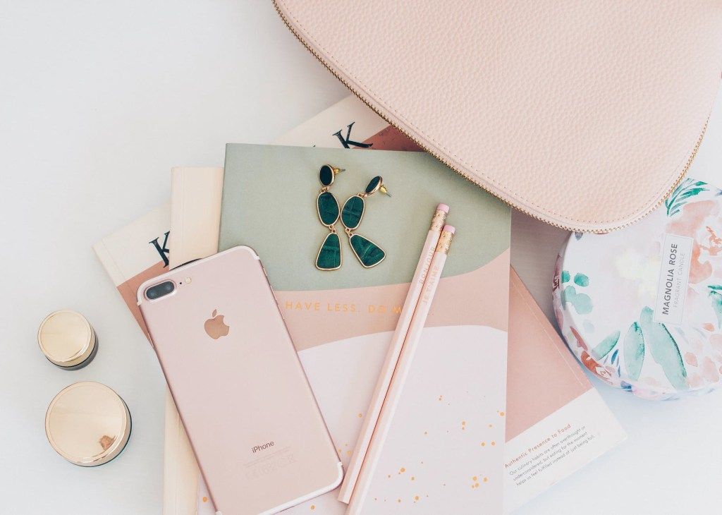 Pink phone, cosmetics, and accessories arranged on a desk