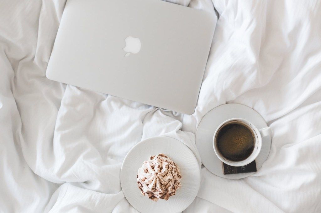 Laptop, coffee, and dessert on white bedding