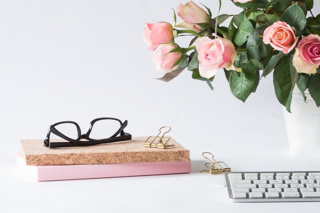 Glasses, books, keyboard, and pink roses on a white desk