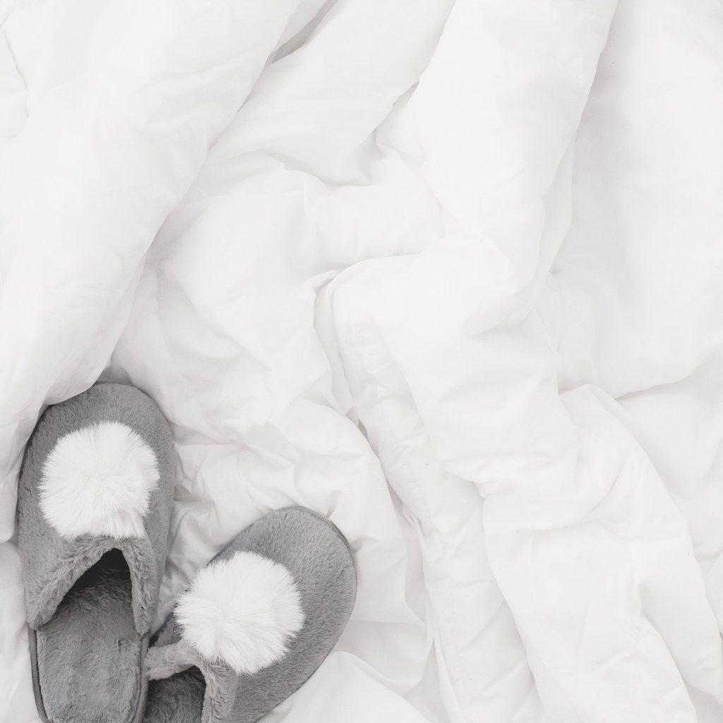 Gray slippers with white pom-poms on rumpled white bedding