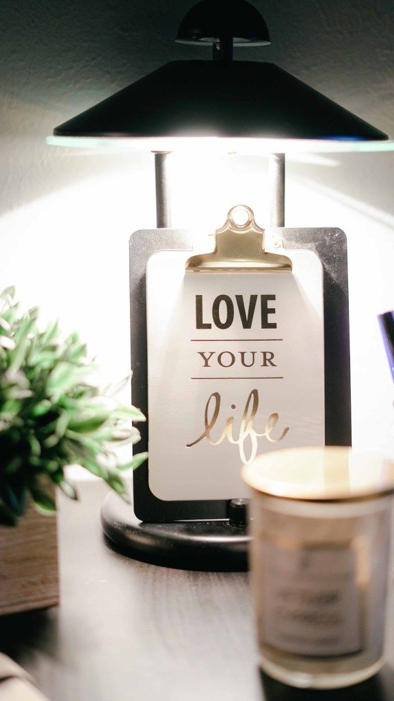 Clipboard reading “Love your life” beneath a desk lamp
