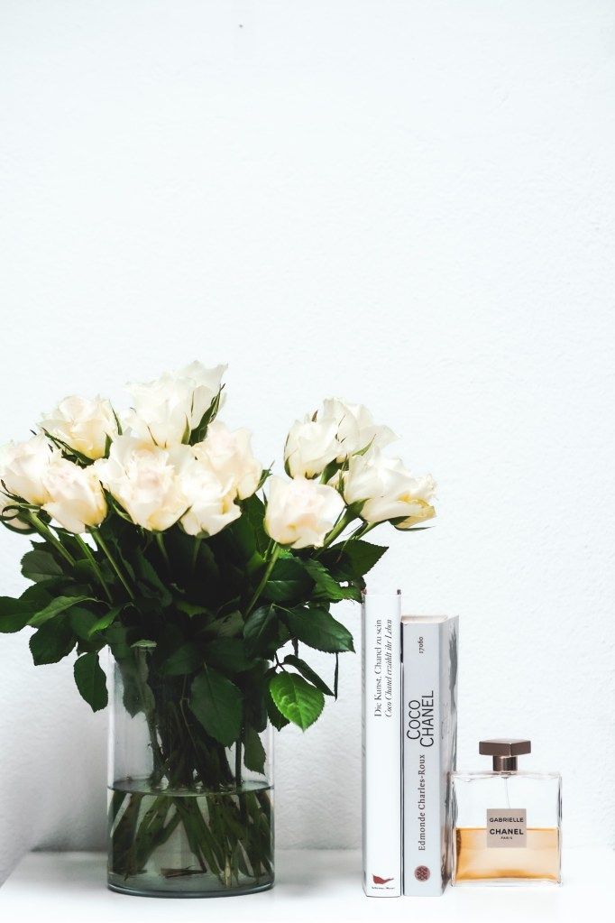 White roses, books, and perfume arranged on a shelf