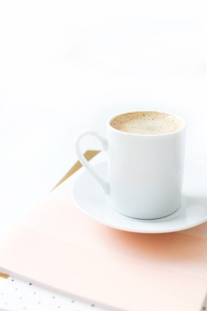 White coffee cup on a saucer atop a pale pink notebook