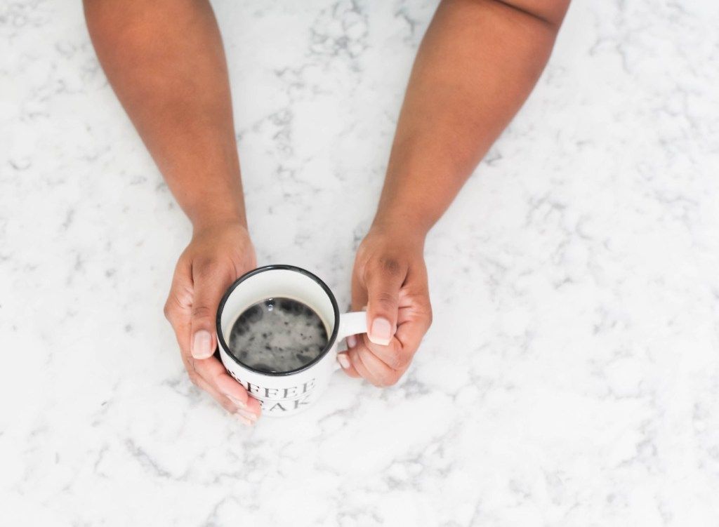 Hands holding a coffee mug over a white marble surface